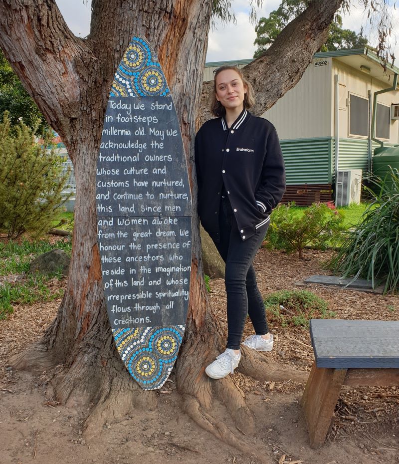 A Brainstorm Productions actor standing next to an acknowledgment of Country at Bulli Public School.