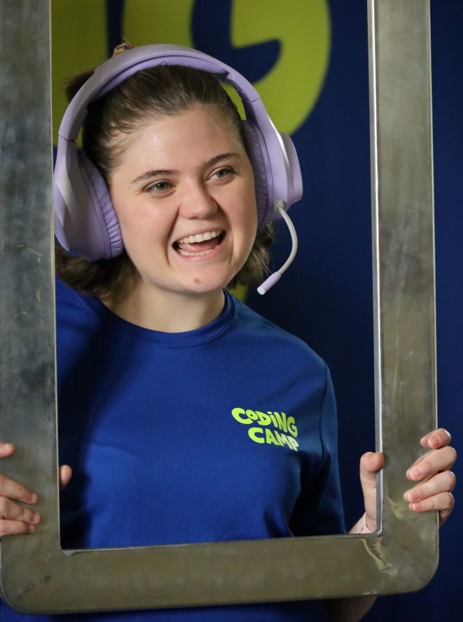 A girl is wearing a gaming headset and smiling, holding a frame around her face. A promo image from Zanna and the Lost Code by Brainstorm Productions.