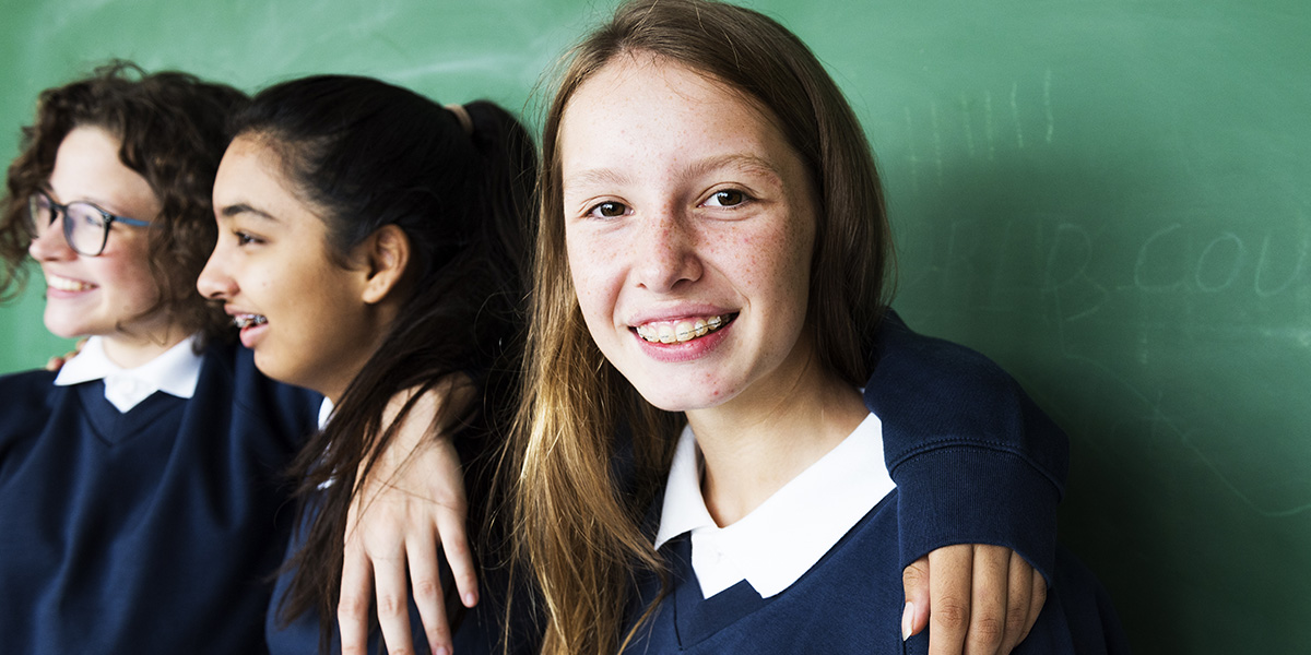 Three female students have their arms around each other and one is smiling at the camera