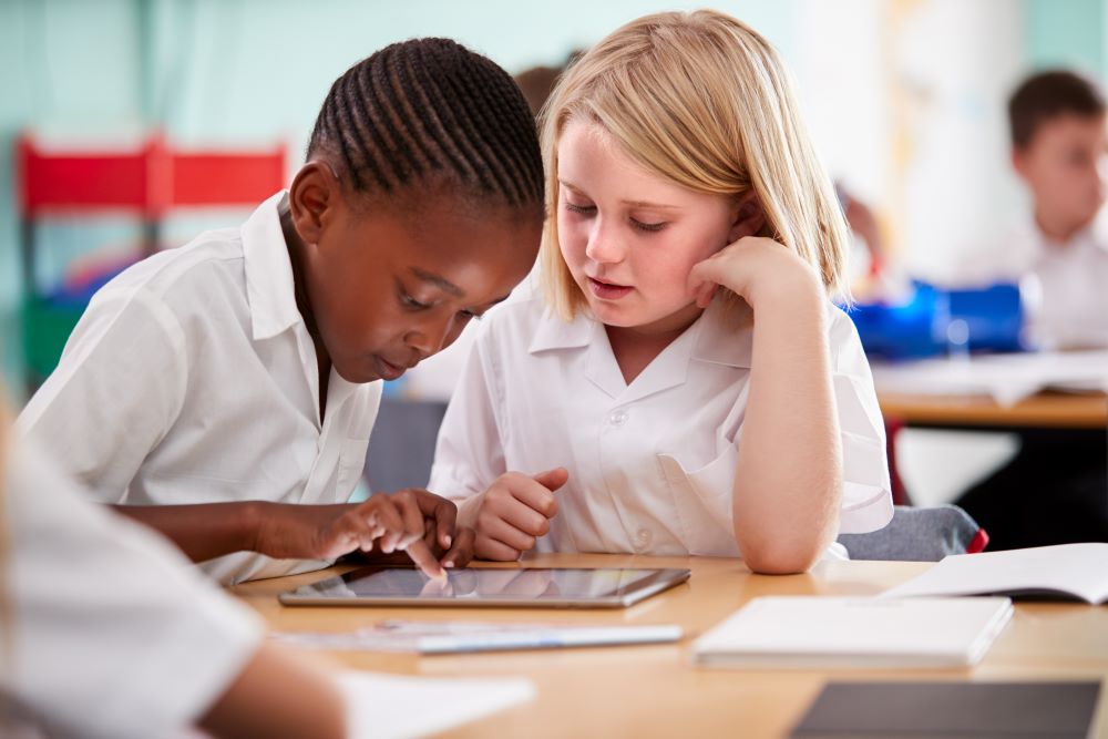 Two primary school students are using a tablet together in a classroom