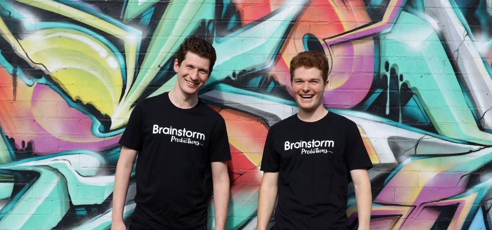 Two Brainstorm actors smiling in front of a colourful street art wall