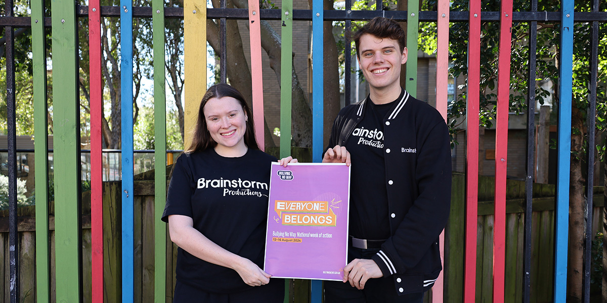 Two Brainstorm Productions actors holding a poster for the Bullying No Way National Week of Action that says 'Everyone Belongs'