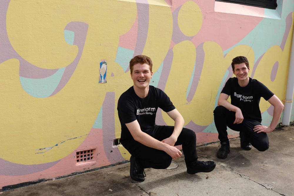 Two Brainstorm actors crouching down in front of a mural that says 'Kind' to promote kindness and antibullying in schools