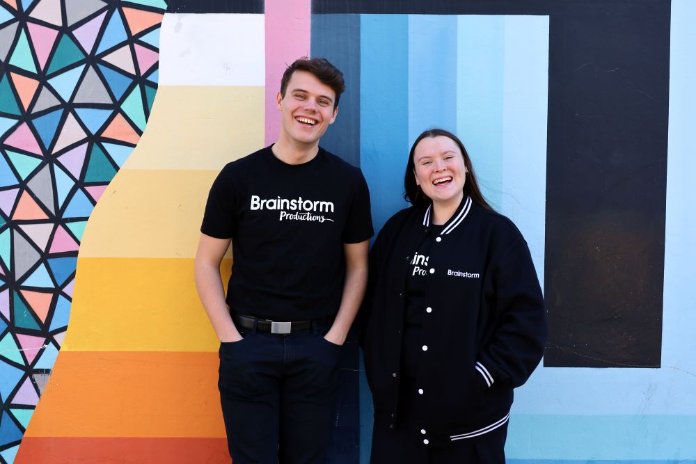 Two Brainstorm actors in front of a mural by street artist Brad Eastman