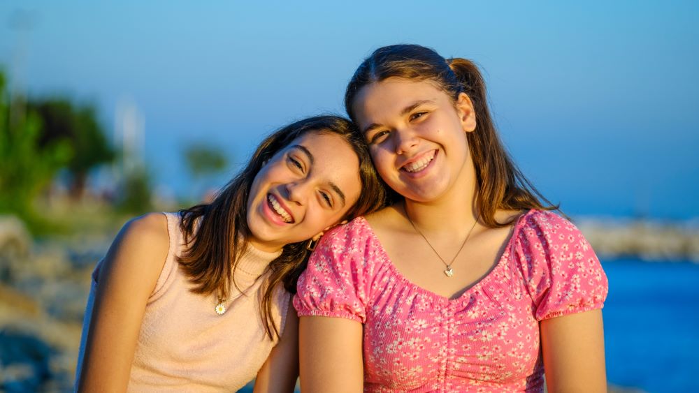 Two teenage girls sitting together and smiling outdoors