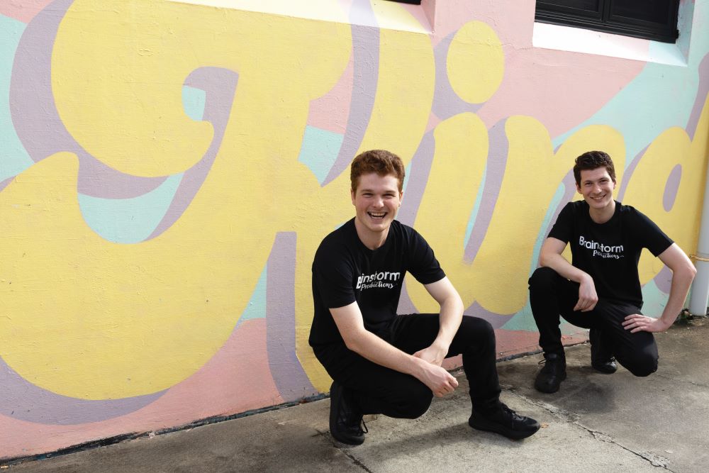 Two Brainstorm productions actors in front of a mural that says 'Kind'