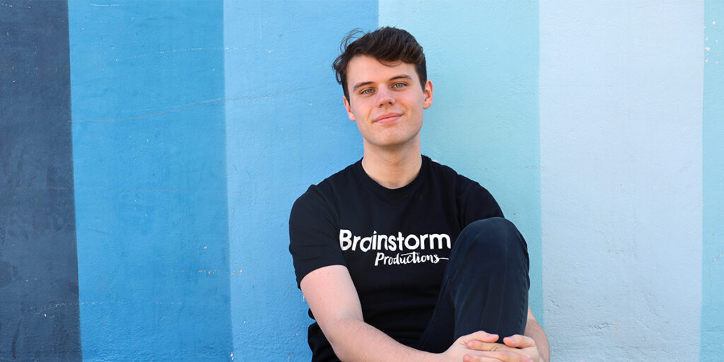 A Brainstorm Productions actor sits in front of a blue painted wall