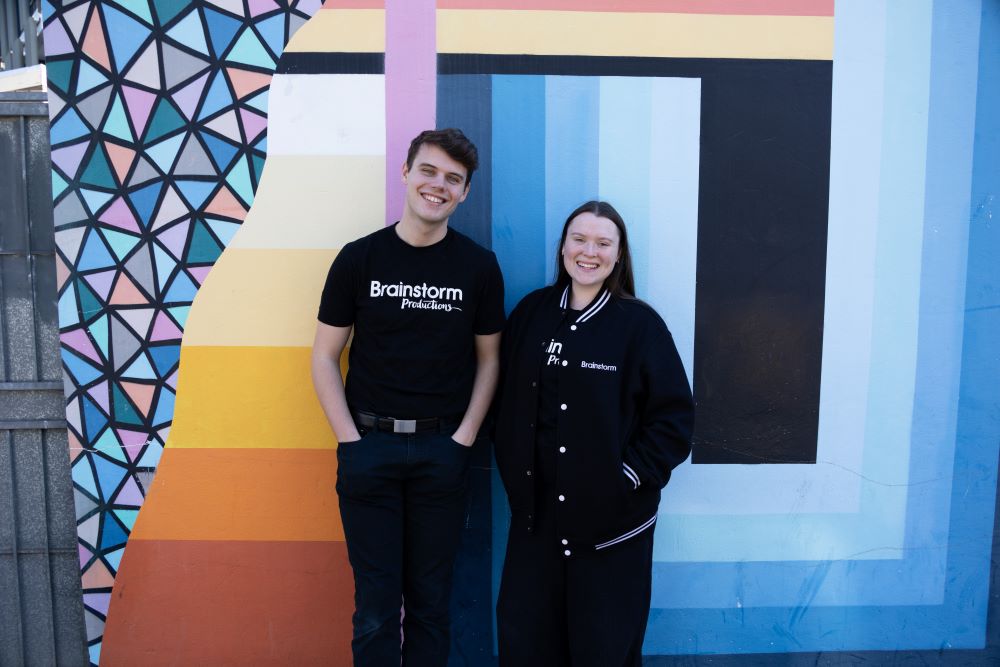 Two Brainstorm Productions actors are smiling in front of a colourful street art mural